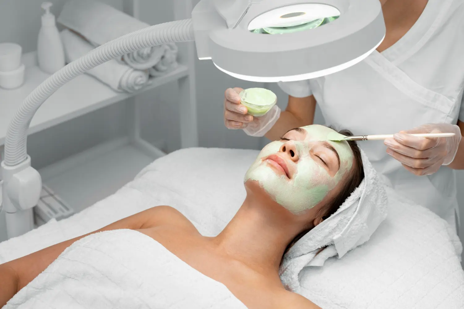 Beautician applying face mask on female client Beautician applying face mask on female client